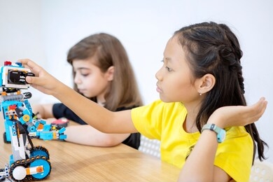 two little girl constructing a lego robot together while sitting in the classroom. shot in the school