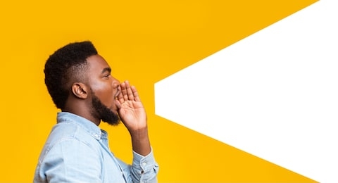 african american man making loud announcement at copy space, holding hand near his open mouth over yellow background, side view