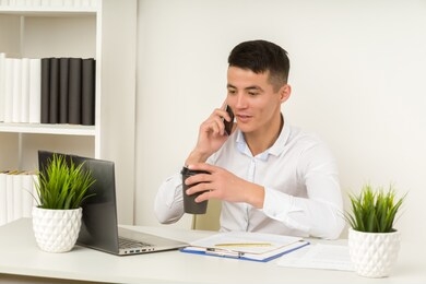 chinese asian business man talking on a mobile phone and working on his laptop in office