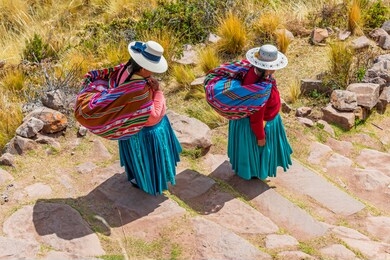 two quechua indigenous women in traditional clothing and textile walking down the steps on taquile island by the titicaca lake, puno, peru.