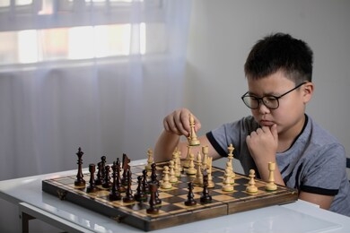 teenager boy playing chess along at the table.