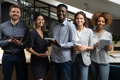 portrait of happy successful multiracial business team standing with digital tablets, notebooks, ready to make notes. smiling young motivated startup international employees group looking at camera.