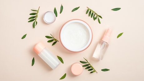 organic cosmetic bottle containers and jar with white face cream on beige background with green herbal leaves. creative layout, minimal flat lay style composition. natural beauty product concept.