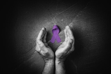 hands holding purple ribbons top view on dark gray background. alzheimers disease, epilepsy, fibromyalgia awareness, world cancer day. black and white. symbol of fighting child abuse.