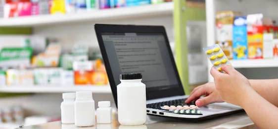 pharmacist using the computer laptop in chemist shop or pharmacy drug store. hand holding medicine pack and key the prescription order.