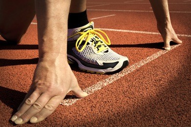 runner in a stadium is in start position with hands on the line