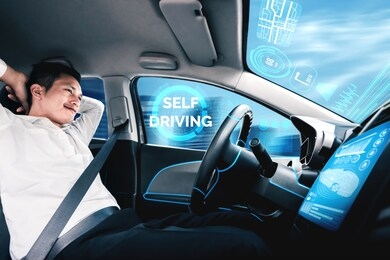 self-driving autonomous car with relaxed young man sitting at driver seat is driving on busy highway road in the city. concept of machine learning, artificial intelligence and augmented reality.