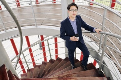 handsome young asian businessman with coffee cup standing on stairs in office building