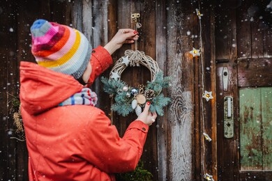 rear view young female hipsters decorate home for christmas door outside. beautiful christmas tree wreath old wooden rustic background. girl red jacket and a striped hat and scarf. new year 2020