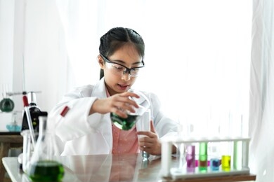 teenage girl students learning and doing a chemical experiment and holding test tube in hands in science class on the table.education concept
