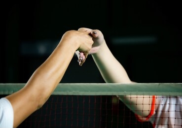 rival badminton players shaking hands over badminton net after match with blurred background