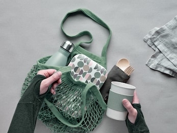 zero waste packed lunch kit in mesh bag. cotton net bag with metal water bottle, bamboo cutlery, bamboo lunch box and reusable cup. sustainable lifestyle. flat lay, top view on craft paper