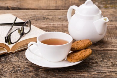 ivory tea cup with sweet cookie, glasses and book on wooden palette