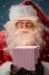 portrait of happy santa claus opening gift box outdoors at north pole. magical light from box on his face