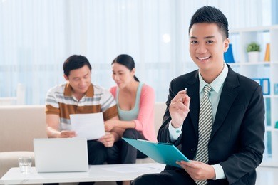 portrait of a young financial broker with a clipboard in hands smiling and looking at camera on the foreground
