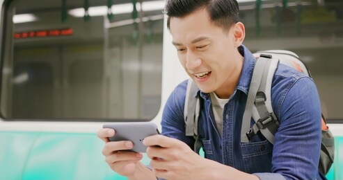 asian young man play game with 5g smartphone in the metro