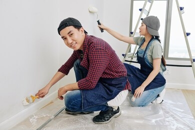 cheerful young asian man painting wall with small brush when his girlfriend using foam roller