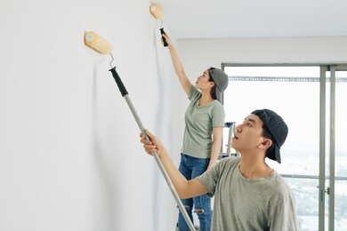 young asian professional house painters in caps using special rolls when painting room walls white