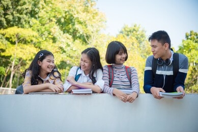 four asian teenager students standing in school and talking with friend happily.