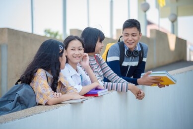 four asian teenager students standing in school and talking with friend happily.