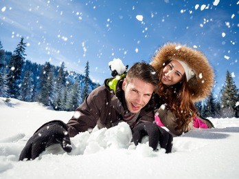 portrait of joyful woman throwing snowball at man