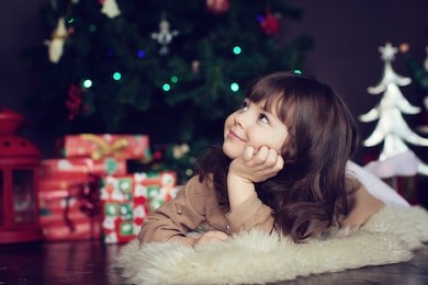 girl with dark hair lying on the carpet. christmas tree in the background. smiles