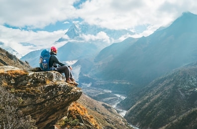 young hiker backpacker female sitting on the cliff edge and enjoying ama dablam 6,812m peak view during everest base camp (ebc) trekking route near phortse, nepal. active vacations concept image