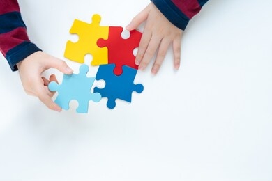 top view hands of a little child arranging color puzzle symbol of public awareness for autism spectrum disorder. world autism awareness day, caring, speak out, campaign, togetherness. isolated.