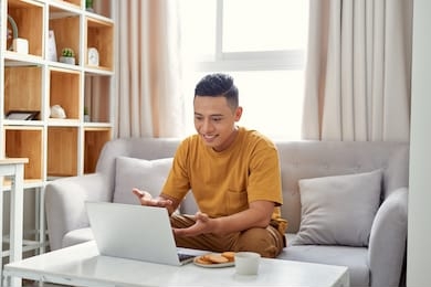 young man is browsing at his laptop and calling with customer on the sofa at home, business success