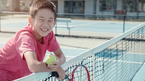 young healthy and happy tween preteen mixed asian boy tennis beginner player on outdoor blue court, active child sport, student school camp
