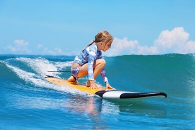 happy baby girl - young surfer ride on surfboard with fun on sea waves. active family lifestyle, kids outdoor water sport lessons and swimming activity in surf camp. beach summer vacation with child.