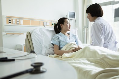 female doctor sitting on hospital bed and discussing with young female patient