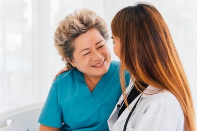 young 30s asian doctor comforts and consoles a happy smiling senior asian woman with gray hair wearing a patient clothing at hospital - healthcare and medical assistance concept