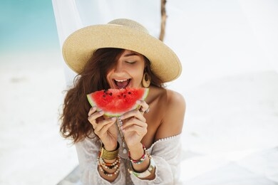 girl holding watermelon on the beach near the water. tropical fruit diet concept. summer holiday idyllic. portrait of happy young mixed race asian caucasian woman with perfect tan at sea resting