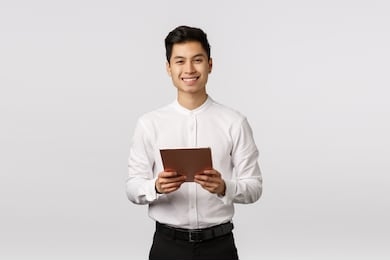 cheerful, polite handsome elegant asian guy in white shirt, black pants, holding digital tablet and smiling camera, using gadget for work, messaging using device, shopping online, white background