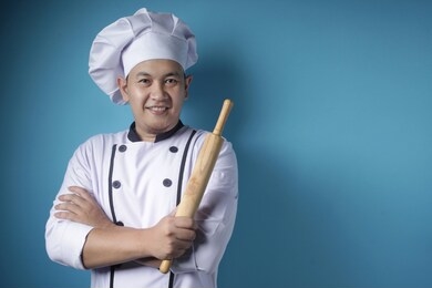 portrait of asian male chef smiling happy while holding kitchen tool rolling pin,  baker ready to cook, against blue background