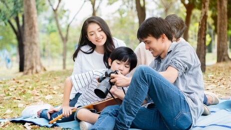 asian family come for picnic at the park. there are father, mother, son and grandmother. there is a nature that makes you feel relaxed and happy. father teaches to use camera for children. copy space