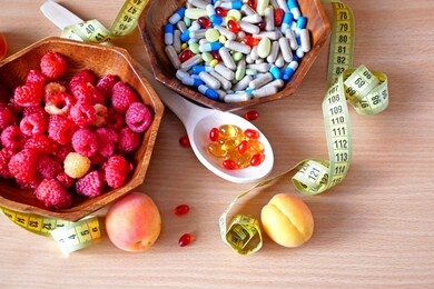 pills and capsules in wooden spoon and fresh tasty fruits on wooden background. nutrition multivitamins and supplement from fruits. organic food instead of pills concept. diet concept. top view