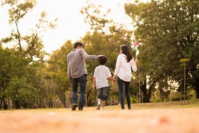 scene from behind of asian happy family spend time together walking and relaxing at the park in the afternoon autumn, concept family togetherness, warm hearted family, parenthood, happy family outing.