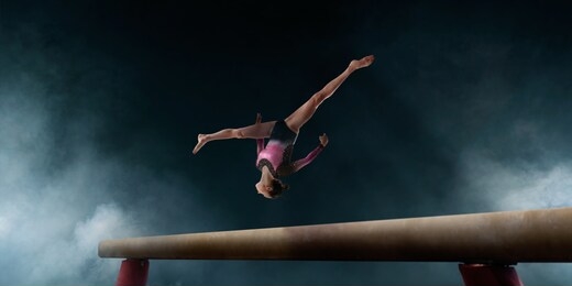 female gymnast doing a complicated trick on gymnastics balance beam.