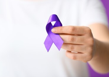 woman with purple ribbon as symbol of world cancer day, closeup