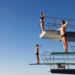 three divers standing on diving boards