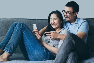 using cell phone couple asian lover happy enjoy sitting on sofa at home looking on mobile laugh and smiling together search information from internet.concept for technology contact communication