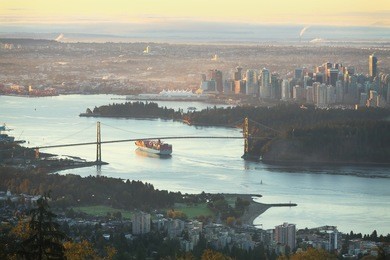 a high angle view of downtown vancouver, the lions gate bridge, and burrard inlet at sunrise. a freighter passes under the bridge as the sun comes up. british columbia, canada.