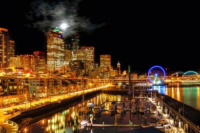 seattle night view of the illuminated waterfront and skyline under a full moon breaking through clouds