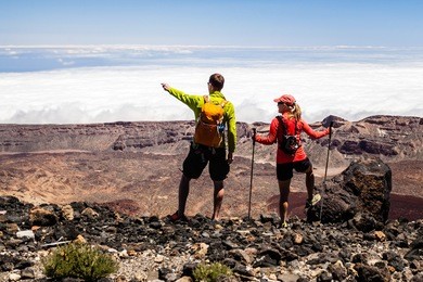 man and woman hikers trekking in summer mountains. young couple on rocky mountain ridge looking at beautiful view. hiking on volcano mountain over clouds, tenerife canary islands
