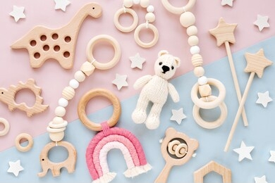cute wooden baby toys on pink and light-blue background. knitted bear, rainbow, dinosaur toy, beads and stars. eco accessories,  beanbag and teethers for newborn. flat lay, top view