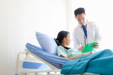 asian male doctor is talking to female patients lie in bed in the hospital room about the diagnosis of her illness.disease treatment and health care concept