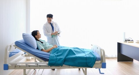asian male doctor is talking to female patients lie in bed in the hospital room about the diagnosis of her illness.disease treatment and health care concept