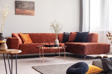 real photo of a rose gold table in warm living room interior with lots of cushions and a corner sofa